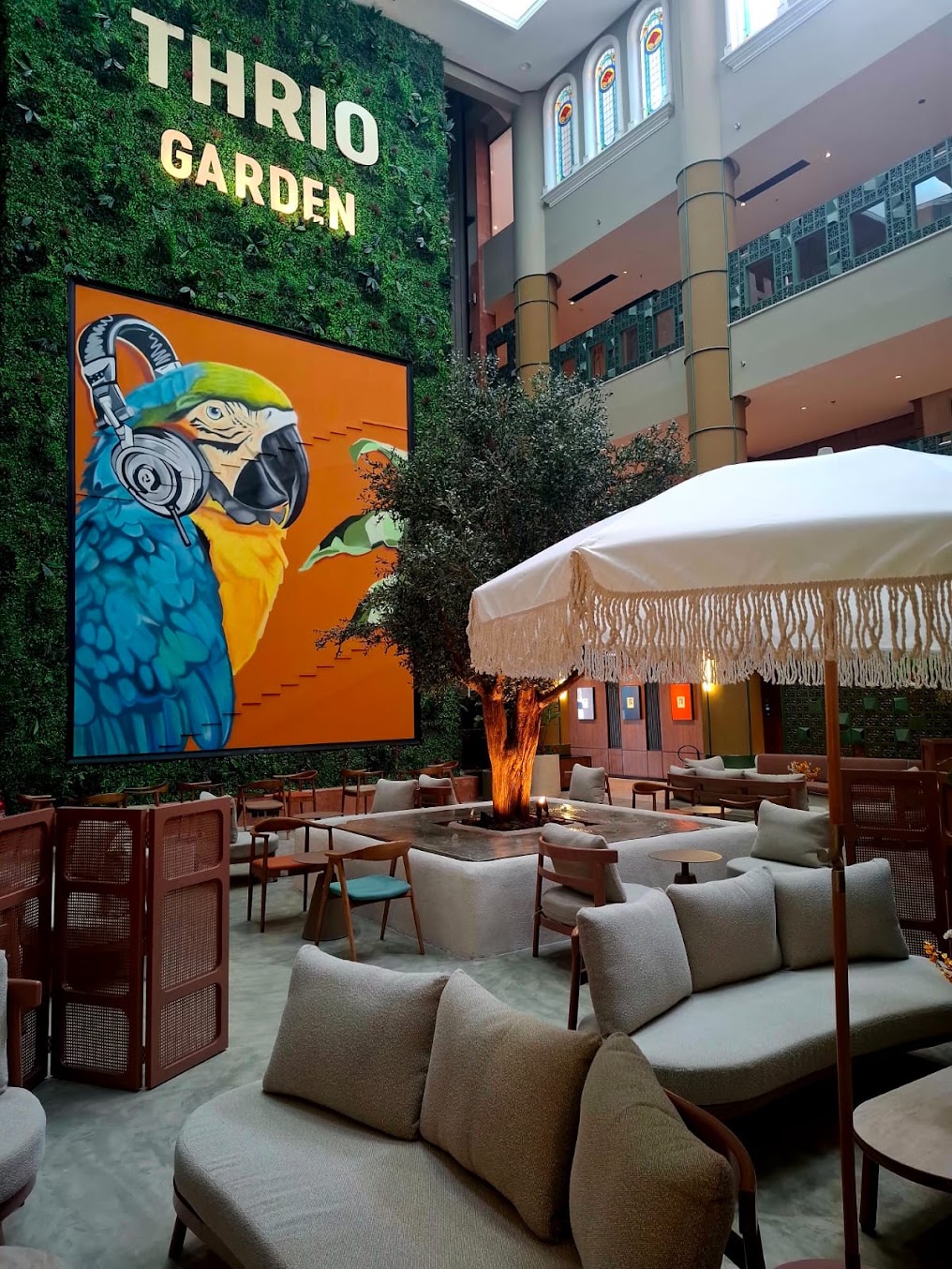 لافتة THRIO GARDEN فوق الجدار الأخضر مع مظلة وجلسات